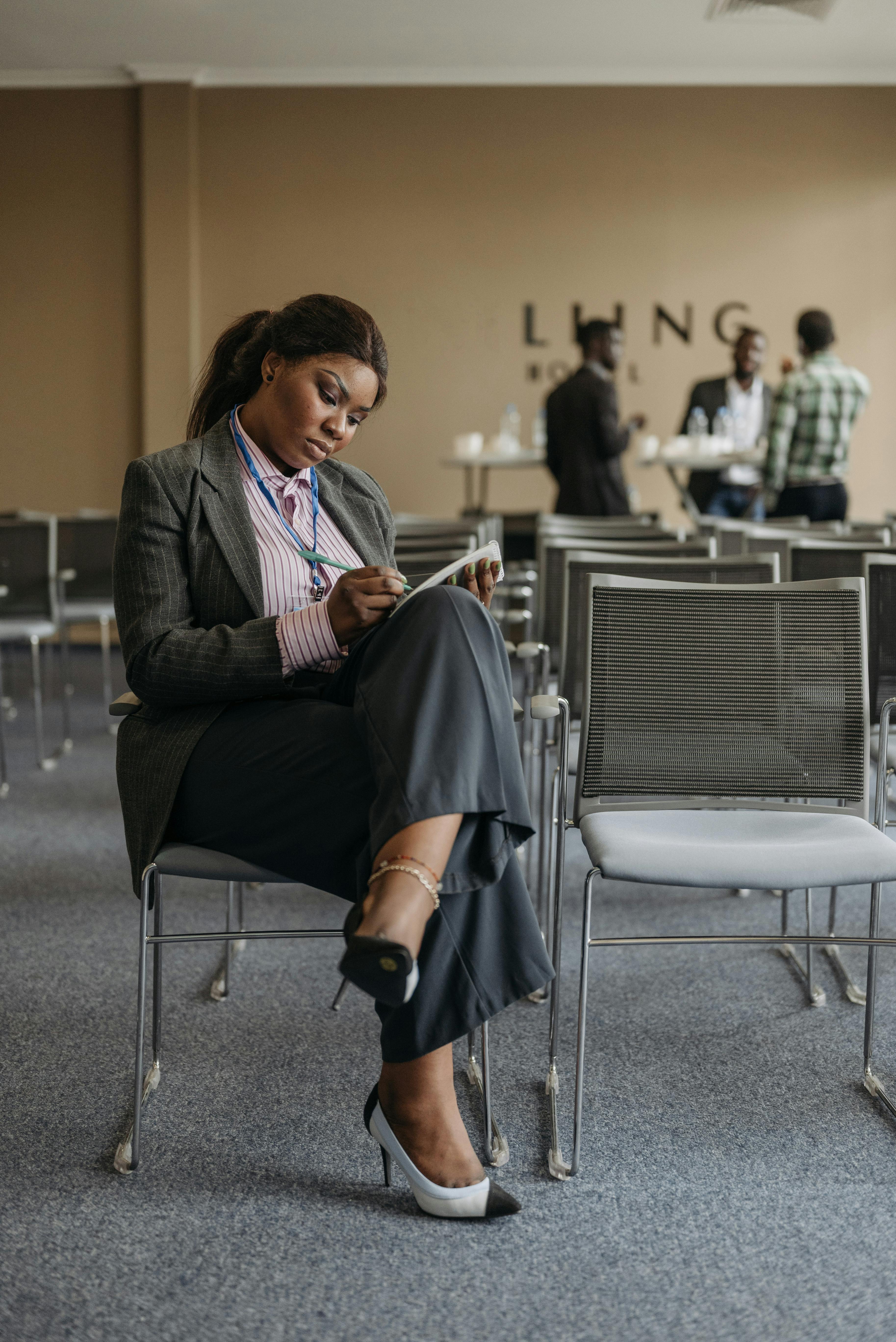 Businesswoman in formal attire writing notes during a conference session.
